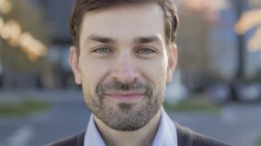 Mutlu ofis çalışanı dışarıda kameraya gülümserken fotoğraflandı. Sonbahar arkaplanı ve doğal ışık sıcak ve davetkar bir atmosfer yaratır..