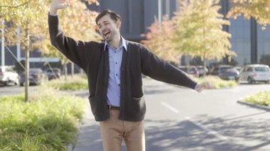 Heyecan dolu neşeli bir ofis çalışanı, modern bir binanın önünde dans ederek başarılı bir iş başarısını kutluyor, zafer anı yakalıyor..
