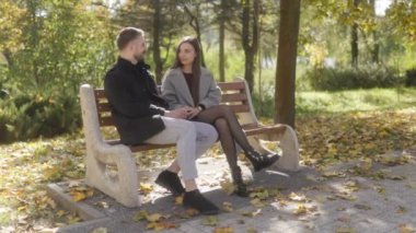 Genç aşıklar sonbahar parkında rahat bir anın tadını çıkarırlar. Güzel sonbahar renkleri ve manzarayla çerçevelenmiş neşeli bir sohbete girişen çift gülümsüyor..