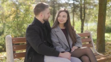 Sonbahar yapraklarıyla çevrili genç bir çift, parkta bir bankta samimi bir kucaklaşmayı paylaşıyor. Doğal ortam, bu romantik açık hava sahnesinin samimiyetini arttırıyor..