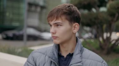 Odaklanmış genç bir çocuk, gelişigüzel giyinmiş, şehir manzarasına karşı duran yakın plan bir portrede, kendine güveni şehir atmosferine iyi uyum sağlıyor..