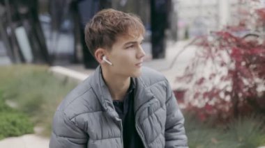 Şehirde genç bir çocuk bir kulaklığını çıkarıp elinde akıllı bir telefonla kameraya bakıp modern bir şehir geçmişine sahip müziğin tadını çıkarıyor..