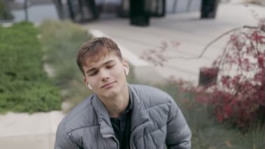 Genç bir çocuk, kablosuz kulaklıkla bir şehir zeminine karşı müzik dinleyerek, kaygısız bir yaşam tarzını ve modern teknoloji tarzını somutlaştırarak bir an rahatlıyor.