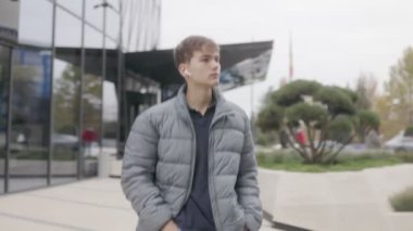 Sıradan ve memnun, genç bir çocuk şehirde yürüyor, kablosuz kulaklıklarıyla müziğin tadını çıkarıyor. Rahatlamış, boş zamanlarının kıymetini biliyor..