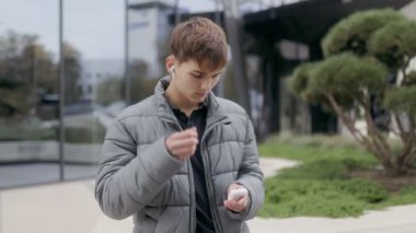 Şehir ortamında genç bir çocuk, kablosuz kulaklığını çıkarmak için duruyor. Şehir hayatının arka planında rahat ve düşünceli bir anı yakalıyor..