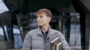 Çalışma materyalleri ve dizüstü bilgisayarı olan bir lise öğrencisi. Üniversite kampüsünde poz veriyor. Arkaplanda yüksek öğrenim görme arzusu vurgulanıyor..
