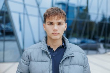 Tarafsız bir ifadeyle genç bir çocuğun sıradan portresi, şehir zeminine karşı duruyor, gençlik hayatının ve modern mimarinin özünü yakalıyor..