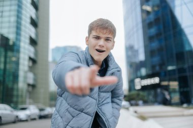 Ergenlik çağındaki erkek kararlı bir bakış açısı ile şehir çevresindeki kameraya bakıyor. Yüksek binalar dinamik bir şehir arkaplanı oluşturuyor..