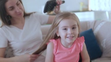 Gülümseyen küçük bir kız annesinin uzun saçlarını rahat bir kanepede taramasından hoşlanıyor. Sıcak bir iç mekanda sevgi, ilgi ve aile bağlarını ön plana çıkarıyor..