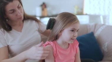 Bir anne, kızına oturma odasındaki koltukta uzun saçlarını tarar ve rahat bir ortamda ebeveyn-çocuk yakınlaşmasının ve aşkın güzel bir anını yakalar..
