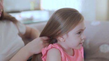 Oturma odasında küçük kızının saçını tarayan, sevgi dolu bir evde şefkatli ve şefkatli bir anı paylaşan bir annenin samimi aile sahnesi..