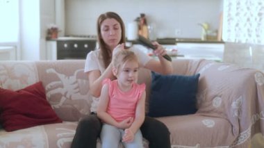 Annesi saçını tararken genç bir kız kanepede annesinin yanında oturuyor. İçten ve sevecen bir aile bağının altını çiziyor..