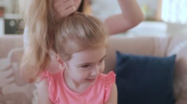 Evde sıcak ve sevgi dolu bir an. Bir anne, kızının saçlarını tarar. Kanepede birlikte oturur ve aile bağının sıcaklığından keyif alır..