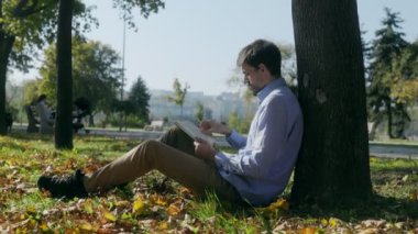 Bir adam bir ağacın altında oturuyor, bir kitaba dalmış, yapraklar onu sarmış gibi. Sonbahar renkleri ve sakin ortam huzurlu ve düşünceli bir anı çağrıştırıyor..
