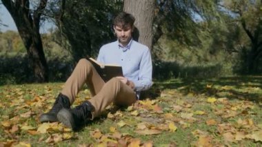 Yumuşak sonbahar güneşinde, bir adam yapraklarla çevrili bir kitapla bir ağaca yaslanır. Odaklanmış ifadesi, sakin ve yalnız bir anın tadını çıkardığını gösteriyor..