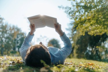 Bir sonbahar parkında çimlere uzanan bir adam kendini bir kitaba daldırır. Sakin ifadesi ve çevreleyen ağaçlar, açık hava rahatlığının basitliğini ve güzelliğini vurguluyor..
