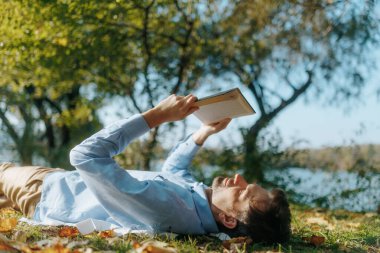 Sessiz, manzaralı bir parkta, bir adam bir kitapla çimlerin üzerinde dinleniyor, bir anlık yalnızlığın tadını çıkarıyor. Sonbahar yaprakları ve güneş ışığı bu kaçıştan zevk aldığı için huzurlu ortamı tamamlıyor..