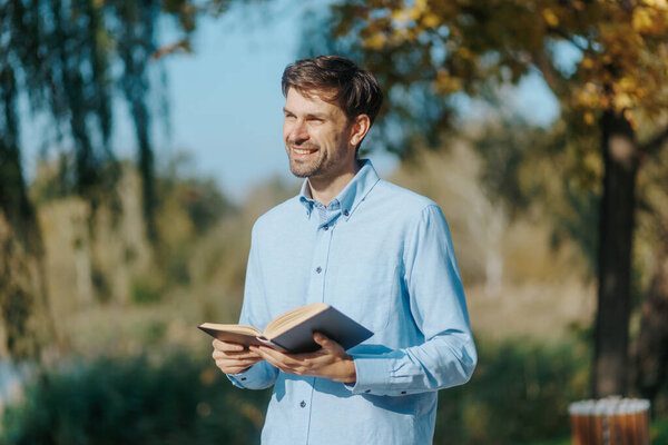 This image depicts a man walking around a park with a book in hand, immersed in his reading. The natural setting offers a tranquil atmosphere for a relaxed outing.
