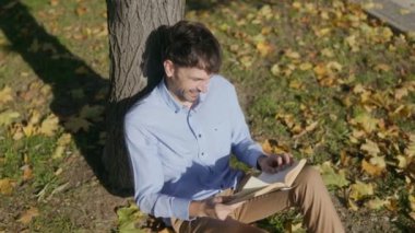 Elinde bir kitapla bir ağacın yanında oturan bu mutlu adam, temiz havayı alıyor, parlak bir şekilde gülümsüyor. Huzurlu ortam onun huzurlu okuma deneyimini arttırır..