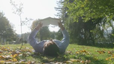 Huzurlu bir park ortamında, bir adam elinde bir kitapla çimenlere uzanıyor, sonbaharın ılık havasının tadını çıkarıyor. Ağaçlar ve düşen yapraklarla çevrili bu sessiz havada huzur buluyor..