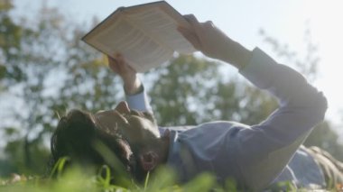 Huzurlu bir sonbahar gününün tadını çıkaran bir adam, canlı ağaçlarla çevrili çimlerin üzerinde yatarken bir kitap okur. Onun rahat duruşu ve odaklanmış ifadesi doğadaki bir anlık sakinliği ve keyfi yansıtıyor..