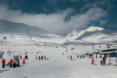 Canlı bir kayak merkezi. Taze kar, bakımlı yamaçlar ve kış sporlarından zevk alan mutlu kayakçılar.