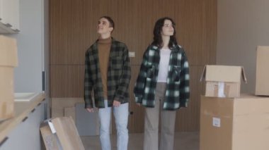Sıradan gömlekler giymiş genç bir çift, karton kutularla dolu yeni bir dairede sarılıyor. İfadeleri gelecekteki evlerini planlama sevincini ve coşkuyu gösteriyor..