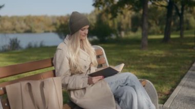 Sonbahar renkleriyle çevrili 30 'lu yaşlarında mutlu bir Amerikalı kadın parkta bir bankta kitap okuyor. Geniş gülümsemesi ve neşeli ifadesi sıcaklık ve memnuniyet saçıyor..