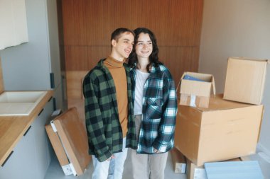 A young family stands together in an unfinished home under renovation, hugging and smiling. Their expressions reflect excitement and love for their future. clipart