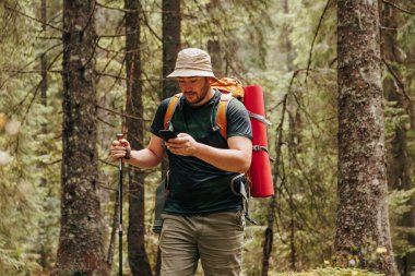 Smartphone Serenity kendinizi doğanın sükunetine sakallı bir yürüyüşçüyle ormanda dolaşırken, akıllı telefonla hazır olun. Görüntü, modern yaşamın kesişimini özetliyor.