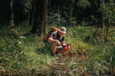 Canlandırıcı Latin Gezgin Adam, bir nehirden su şişesini doldurur ve bir orman dolumu yapar..