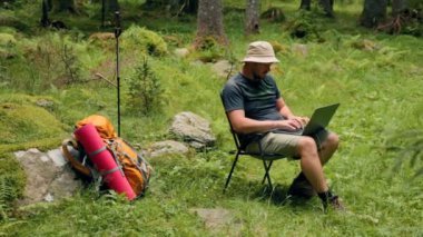 Denge sanatını keşfedin. Bir Amerikan yürüyüşçüsü, dizüstü bilgisayarının talepleriyle sorunsuz bir şekilde hokkabazlık yaparken kendini huzurlu bir doğa yürüyüşünün güzelliğine daldırıyor..