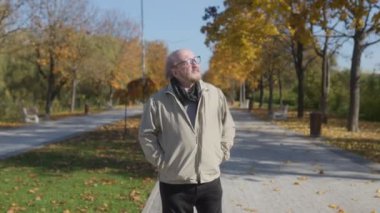 Sakallı ve gözlüklü olgun bir beyefendi bir sonbahar parkında geziniyor, güneşli bir günün dinginliğinin ve huzurunun tadını çıkarıyor mevsimlik renklerin ve yaprakların arasında..