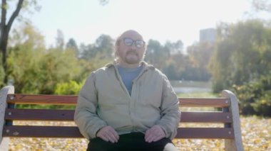 Kıdemli adam sonbahar renkleriyle dolu bir parktaki bankta sakin bir anın tadını çıkarıyor. Huzurlu atmosfer ve doğal çevre bir sakinlik hissi uyandırıyor..