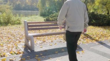 Gözlüklü kıdemli adam, parktaki bir bankta oturmuş, canlı sonbahar yaprakları ve dingin doğayla çevrili bir şekilde yalnızlıktan zevk alıyor..