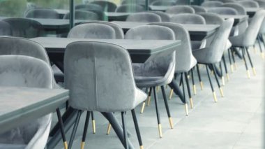 Bir restoranda sıra sıra sandalye ve masalar düzenlenir. Sandalyeler gri, masalar siyah.