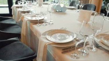 Masada beyaz bir masa örtüsü, birkaç tabak, çatal, bıçak ve şarap bardakları var.