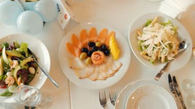 İçinde salata, meyve ve sandviç de bulunan çeşitli yiyecekler olan bir masa. Masa çatal bıçak ve şarap kadehleriyle dolu.