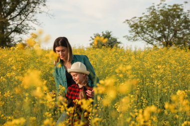 Şapkalı bir anne ve çocuğun ön görüntüsü, gülümseyen kolza tohumu mahsulünü inceler. Çiftliklerinde çalışan bir aile. kırpılmış