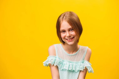 Çocuk mutlu bir şekilde gülümsüyor, sarı saçlarıyla, kameranın önünde tatmin olmuş bir şekilde bakıyor, mutlu. Stüdyonun sarı arka planında güzel bir çocuğun önünde bakmak..