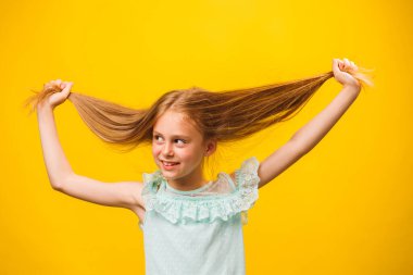 Çocuk sarı arka planda turkuaz bir elbise giyiyor. Kız sola bakıyor. Çocuk olumlu duygular gösteriyor. Çocuk ve kopyalama alanı