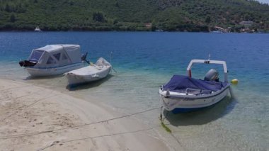 Kıyıya yakın suda üç küçük tekne duruyor. Su sakin ve kayıklar kıyıya bağlı. Sahne huzurlu ve dinlendirici, tekneler de rahatlık hissi veriyor.