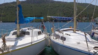 İki küçük beyaz tekne bir su kütlesinin içinde yan yana yanaşır. Tekneler bir rıhtıma bağlı ve mavi yelkenleri var. Sahne huzurlu ve huzurlu, teknelerle.