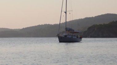 Yelkenli sakin bir gölde yüzüyor. Gökyüzü turuncu ve pembe renklerin karışımıdır. Huzurlu ve huzurlu bir atmosfer yaratır.