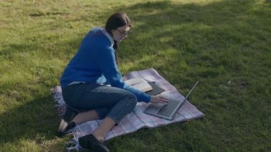 Serin bir sonbahar gününde, genç bir kız parkta çalışır, dizüstü bilgisayarı ve kitaplarıyla çimlerin üzerinde oturur. Odağı öğrenmeye olan bağlılığını vurguluyor..