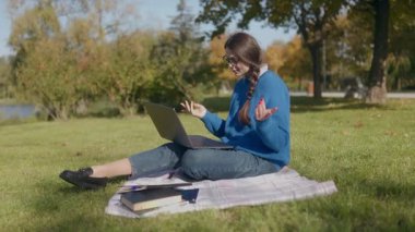 Genç bir kız öğrenci sonbahar parkında çimlerde oturur ve bilgisayarından biriyle konuşur. Etrafı kitaplarla çevrili, çalışıyor ve açık havada online bir sohbete girişiyor..