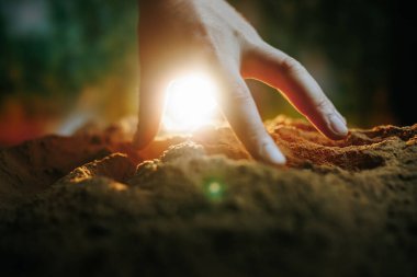 Güneş ışığı toprağı aydınlatırken bir el yavaşça zengin toprağa dokunur. Bu an, şafak sökerken insanlar ve doğa arasındaki bağlantıyı yakalar..