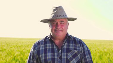 Güneşli bir yaz günü kırsal kesimde tarım çiftliğinde dikilen şapkalı yaşlı, mutlu erkek işçi kırsal kesimde mutlu ve olgun bir çiftçi.