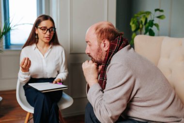İyi ışıklandırılmış, çağdaş bir ofiste bir terapistle konuşurken eşarp takan bir adam dalgın görünür. Terapist özenli görünüyor, destekleyici bir ortam sağlıyor..