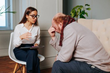 Bir terapist, düşünceli ve sıkıntılı görünen hastasıyla düşünceli bir konuşma yapar. Sıcak iç ve profesyonel ortam destekleyici bir atmosfer yaratıyor..